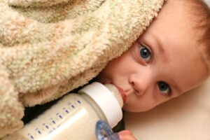 Close up of a blue eyed baby boy drinking his bottle of milk and cuddling with his blanket.