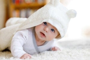 Baby boy with blue eyes wearing white towel or winter overall in white sunny bedroom.