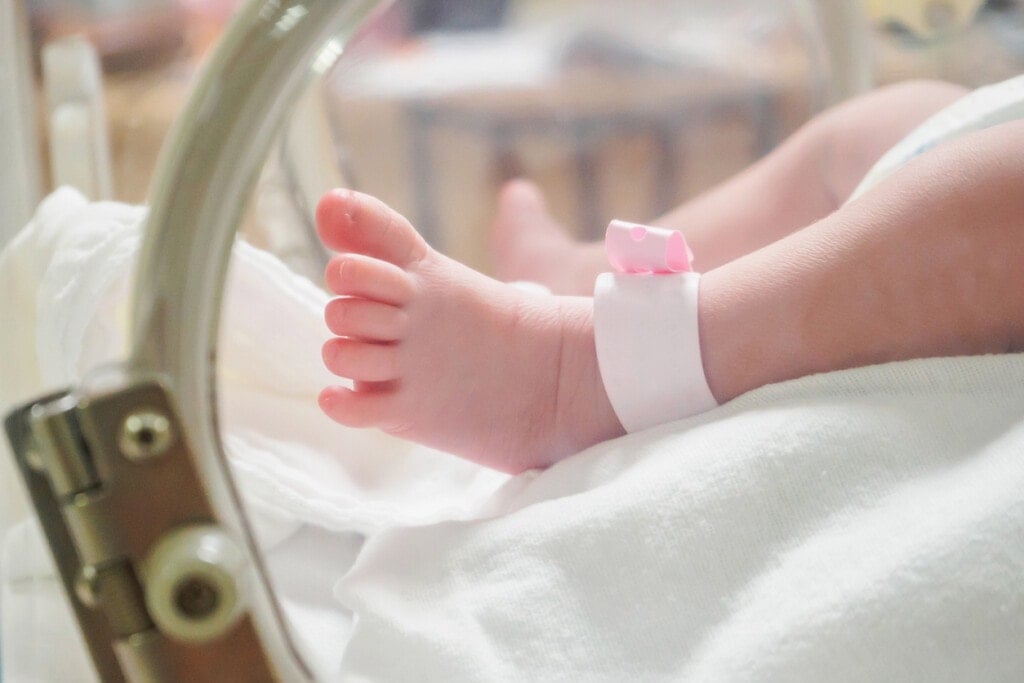 Newborn girl baby inside incubator in hospital post delivery room with identification bracelet tag name