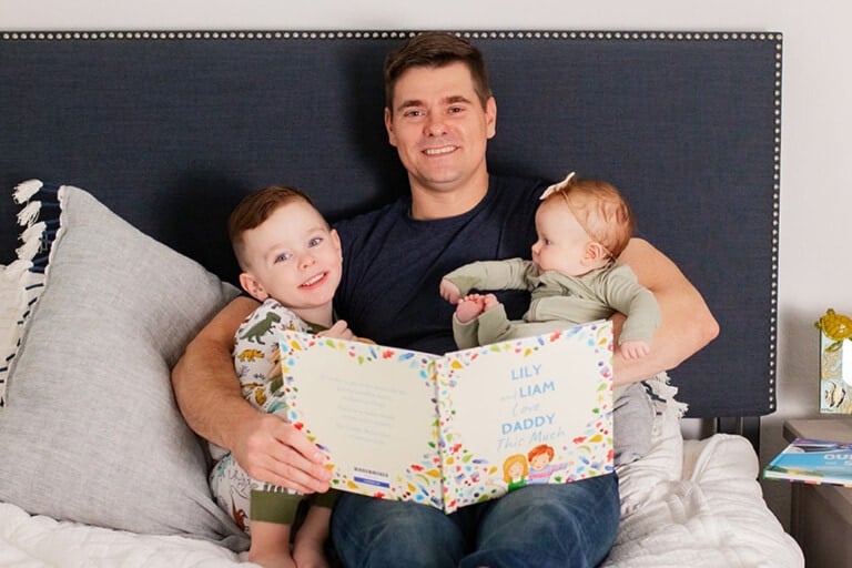 Father sitting in bed with his two children reading a personalized book from Wonderbly he received for Father's Day.