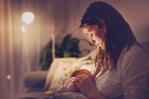 Young beautiful mother, breastfeeding her newborn baby boy at night, dim light.