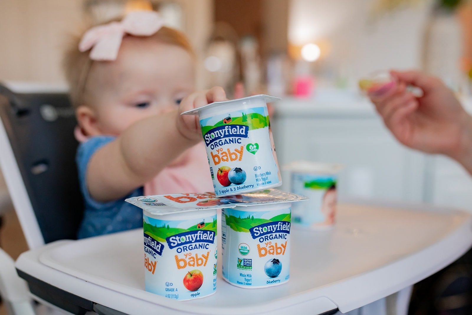 Baby girl reaching out to Stonyfield yogurt cups on her high chair.