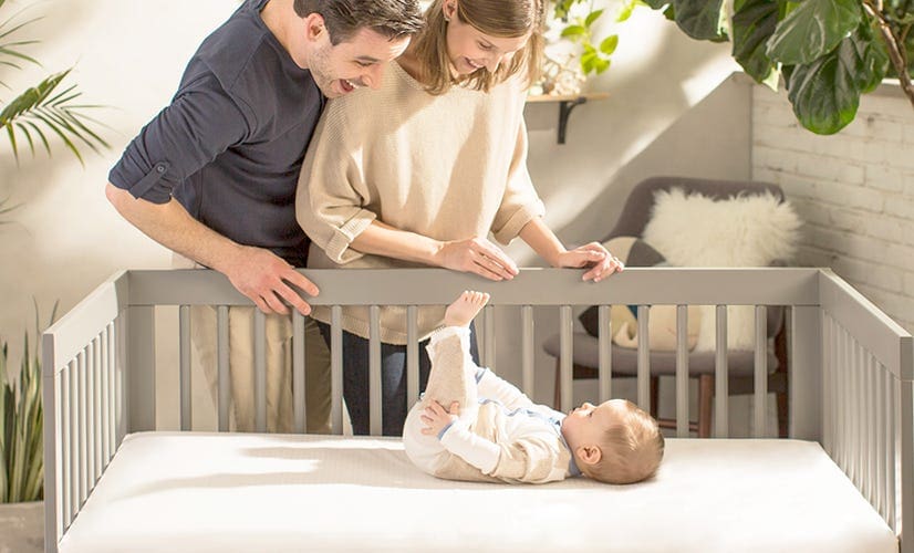 Couple looking at their baby in a crib laying on his crib mattress.