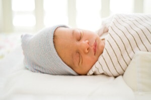 New-born baby sleeping on a bed wearing a blue hat