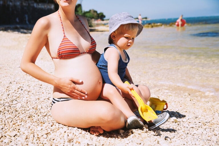 Pregnant mother and her son little cute toddler child playing and relaxing on the sea beach at summer time.