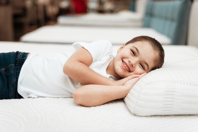 Smiling little girl lies on an orthopedic mattress in a furniture store.
