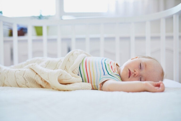 Adorable baby girl sleeping in co-sleeper crib attached to parents' bed. Little child having a day nap in cot. Infant kid in sunny nursery.