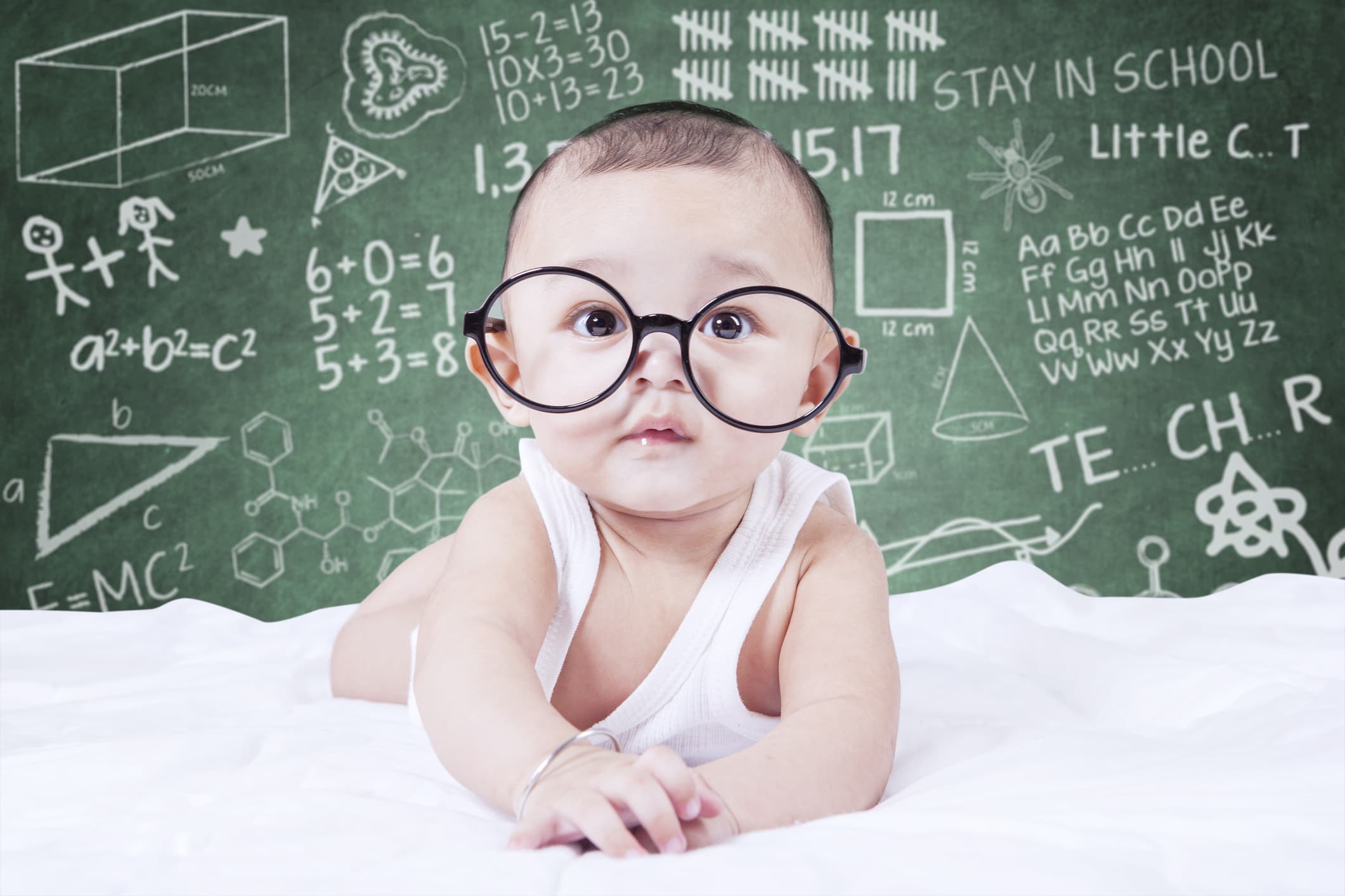 Cute male baby looking on the camera while wearing glasses, shot with a doodles background on the blackboard