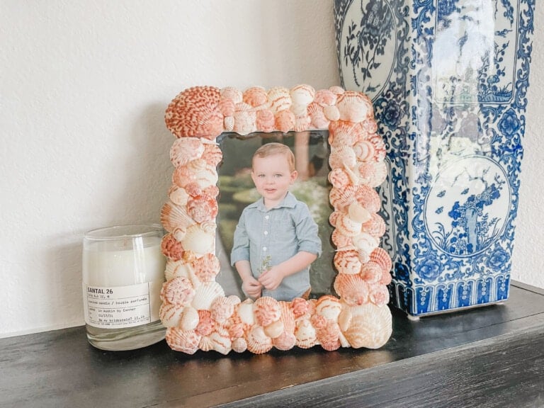 DIY shell frame on a mantel with a candle and vase.