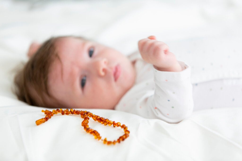 3 month old beautiful, cute baby with amber necklace lying in bed
