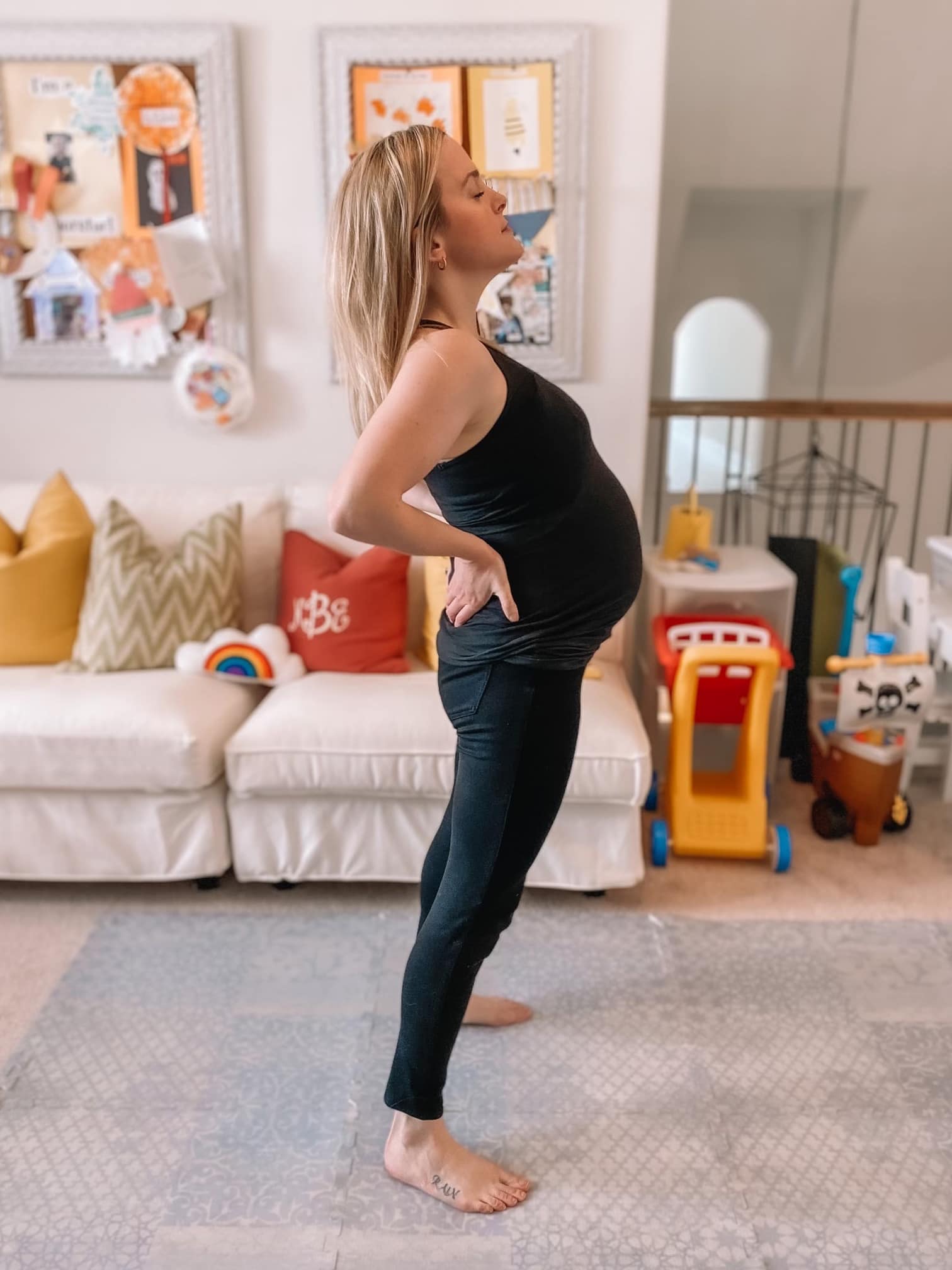 Pregnant woman doing a lower back stretch while standing.