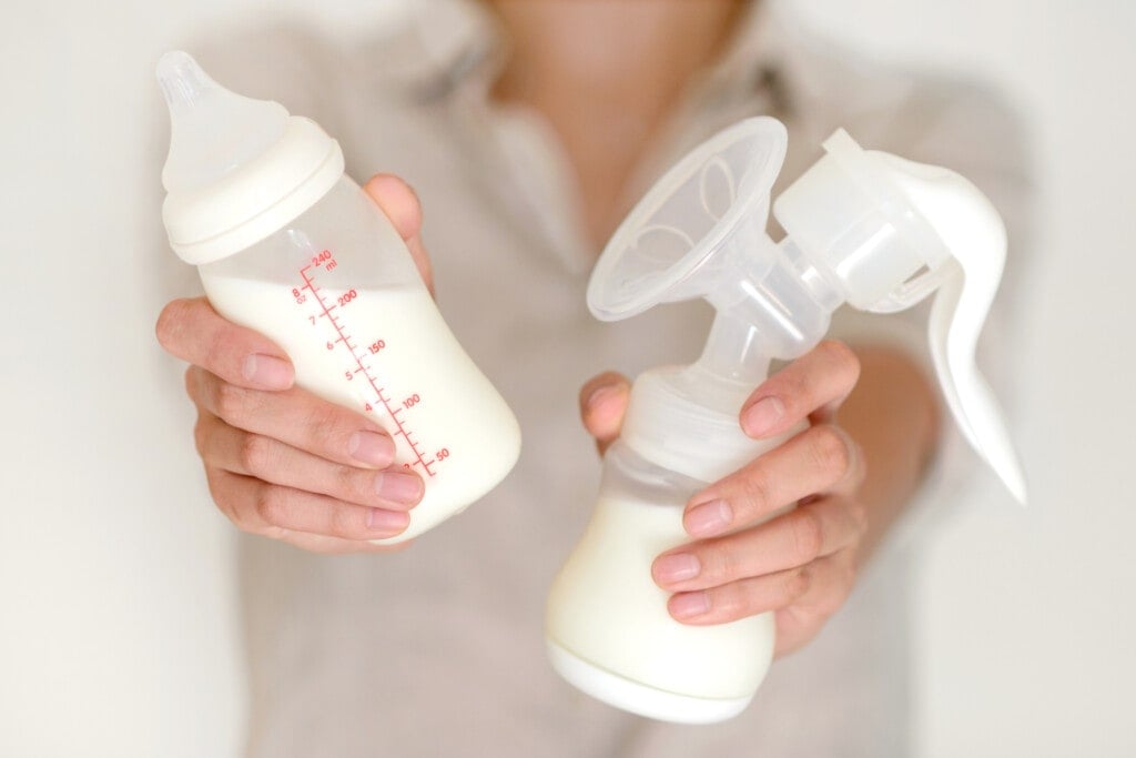Breast pump and bottle with milk in woman's hand in blurred background