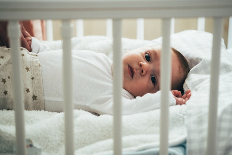 Beautiful little baby boy relaxing in his crib at home.