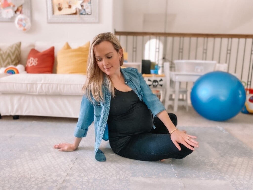 Pregnant woman sitting on the floor stretching her back.