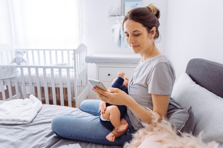 Mother breastfeeding baby son in bedroom and using mobile phone