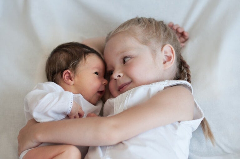 5 years old sister hugs her younger 2 weeks old baby brother.