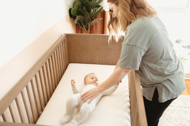 Mother putting her baby down in a safe sleep space on a Naturepedic mattress.