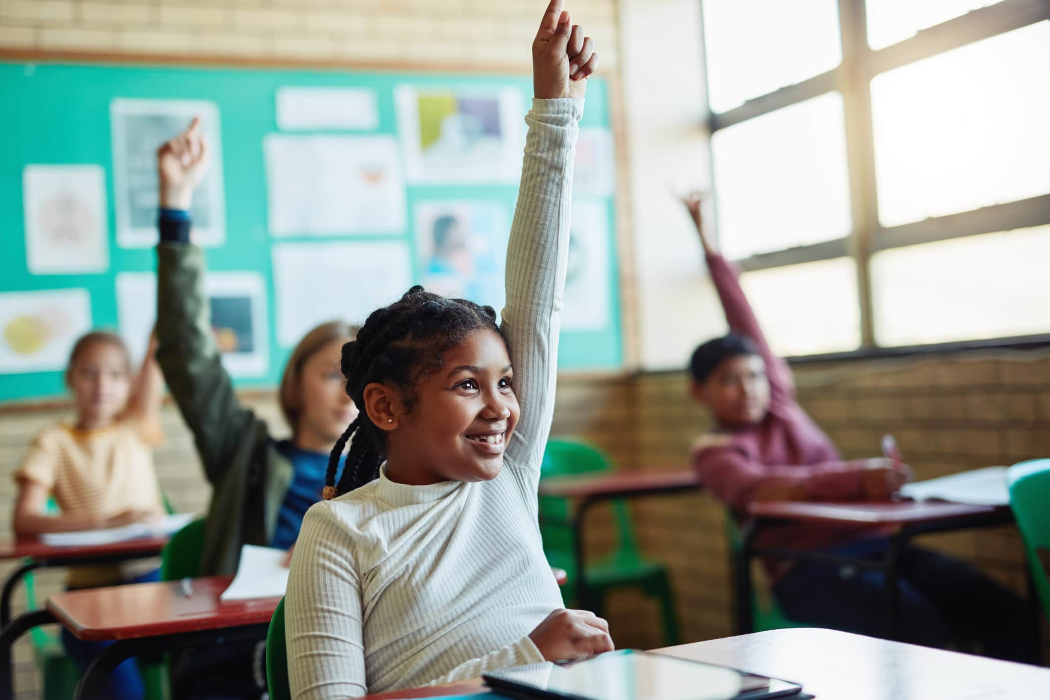 Shot of young children raising their hands in a classroom