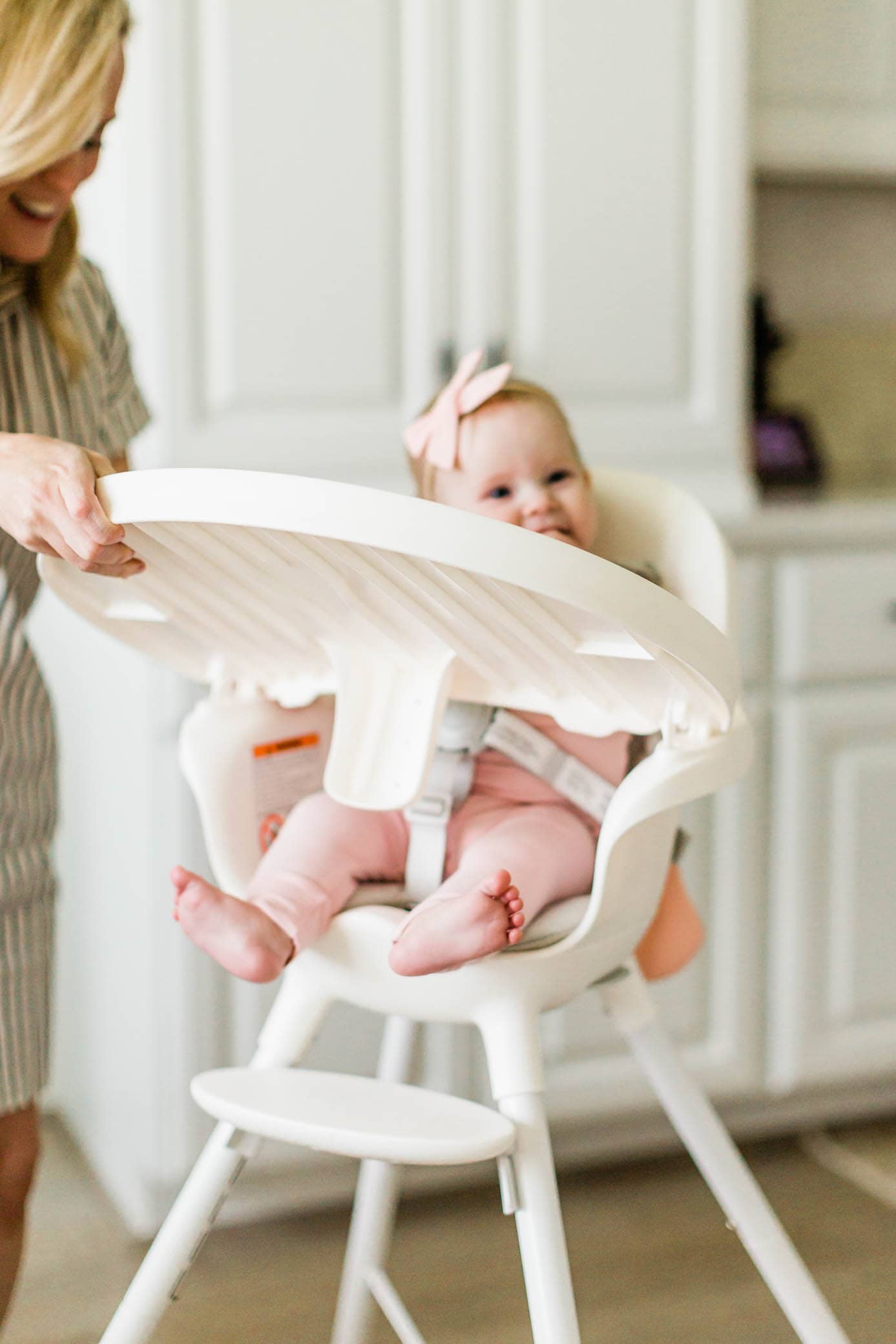 Mom putting her daughter in her high chair and placing the tray in position.