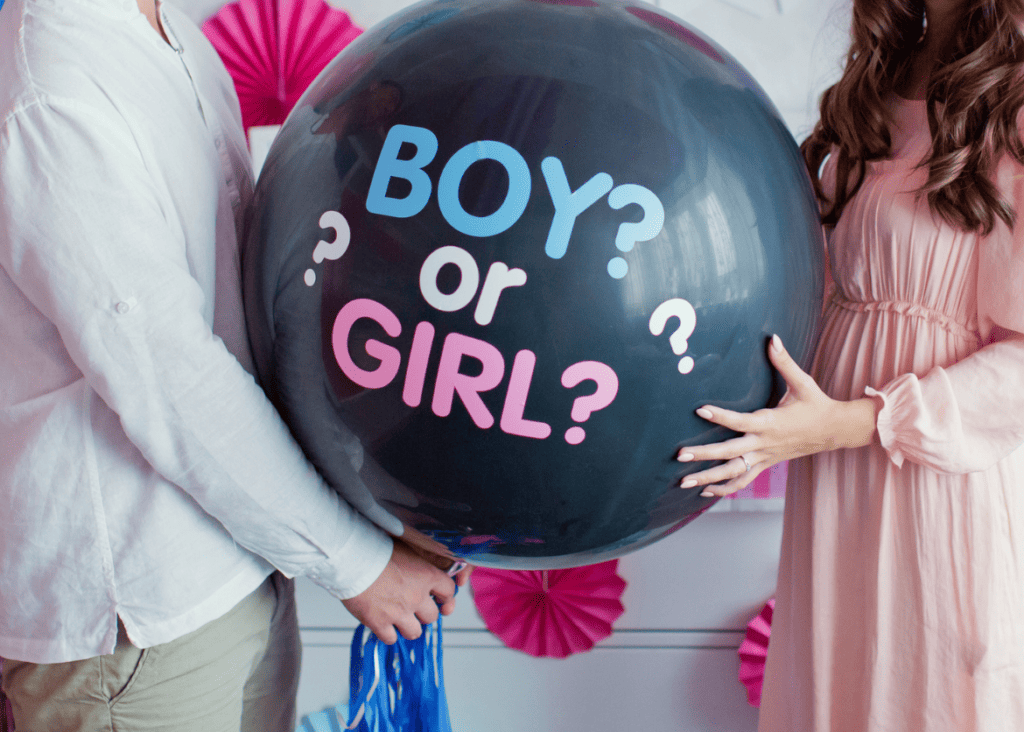 Man and woman holding a big black balloon that says Boy or Girl for their baby's gender reveal.