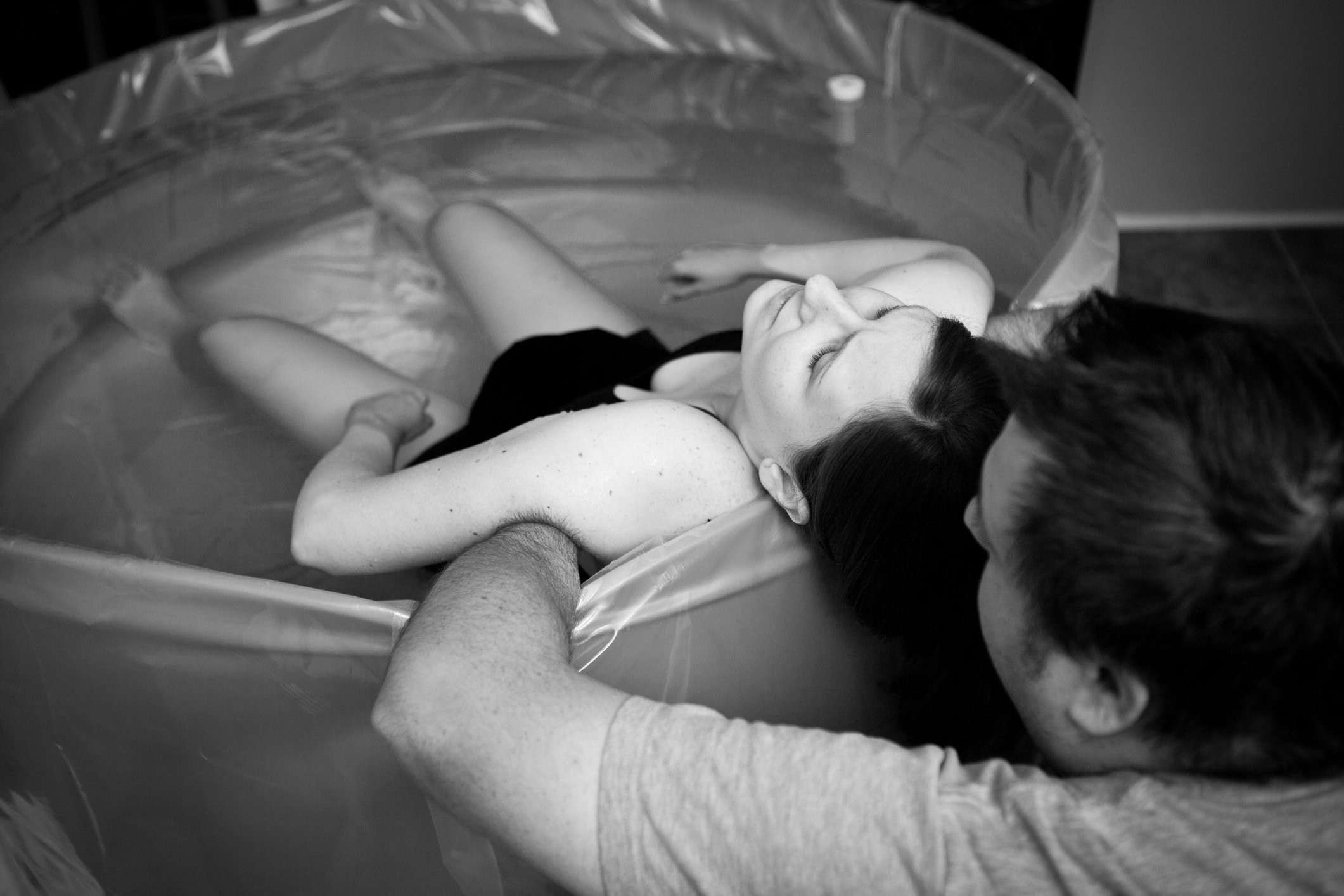 Black and white image of a loving husband supporting and coaching his wife through an intense home birth.