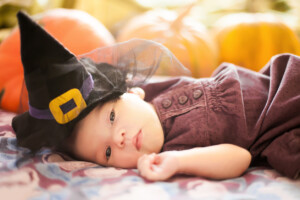 Cute newborn girl wearing witch hat. Orange pumpkins on the background.