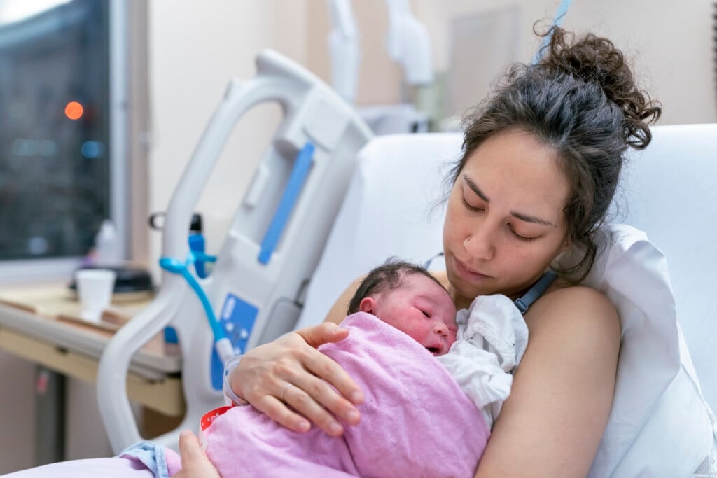 A beautiful and relaxed ethnic mother is snuggling her newborn and affectionately holding her in the hospital after delivery. Skin to skin bonding.