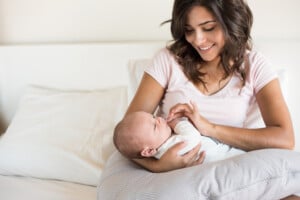 Young mother with baby sitting in bed while baby is supported by a nursing pillow.