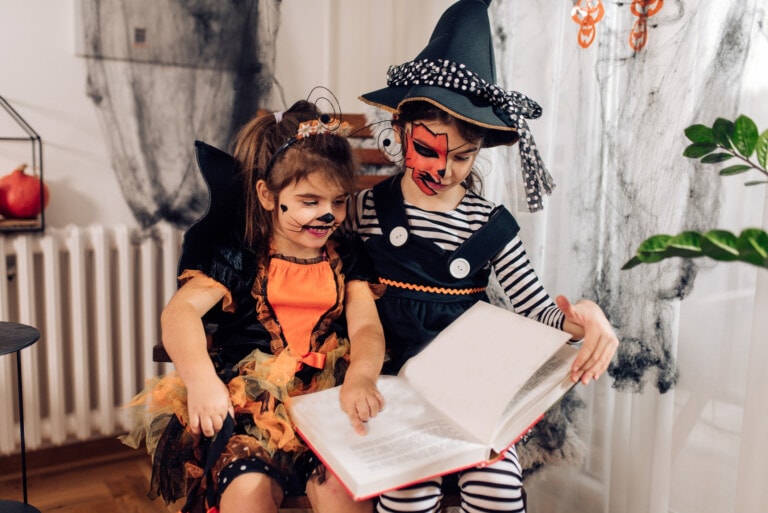 Two cute girls wearing Halloween costumes, playing and reading a book at home.