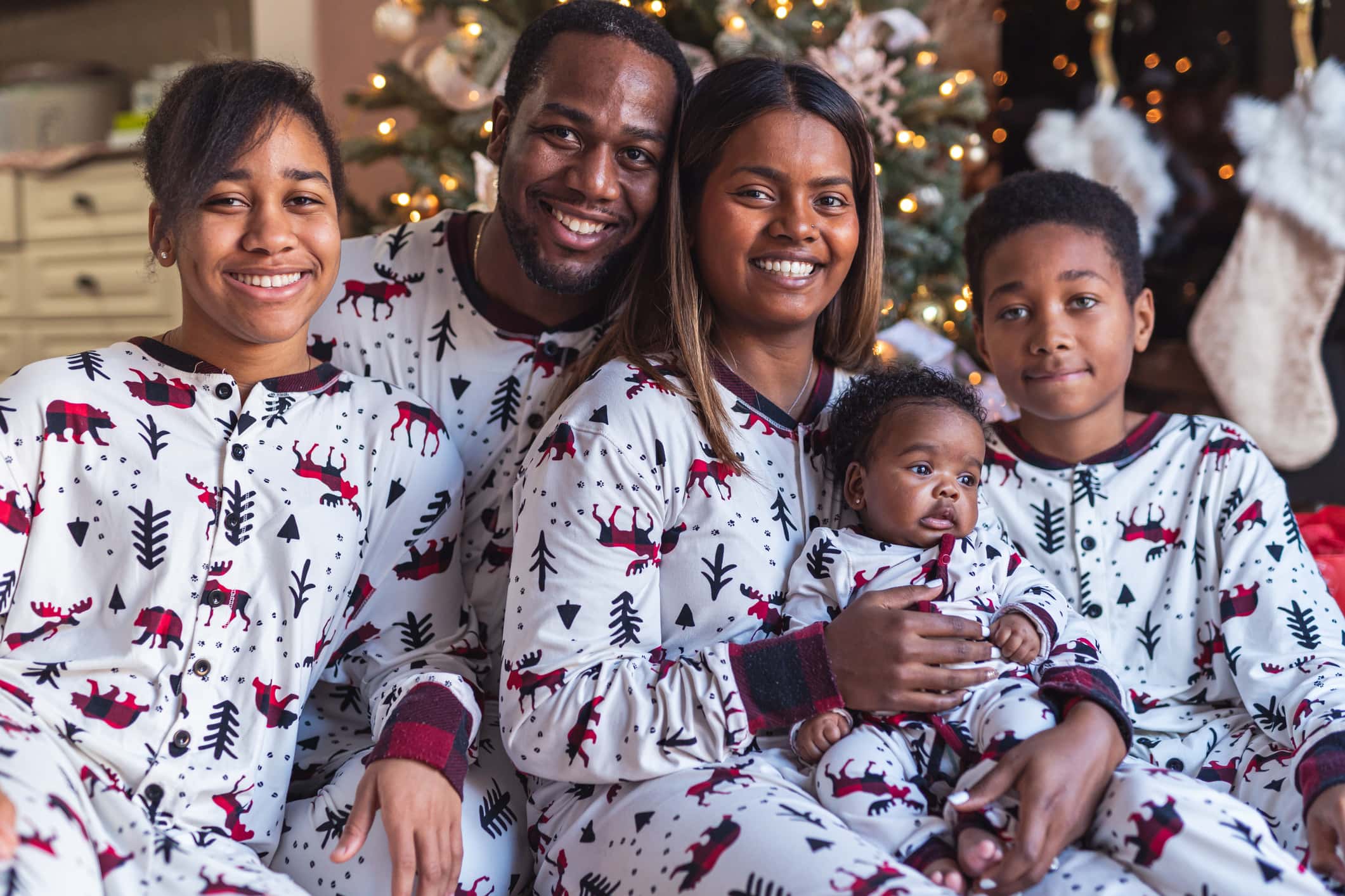 An attractive mixed race family wear matching Christmas pyjamas on Christmas Day. They are looking directly at the camera and smiling.
