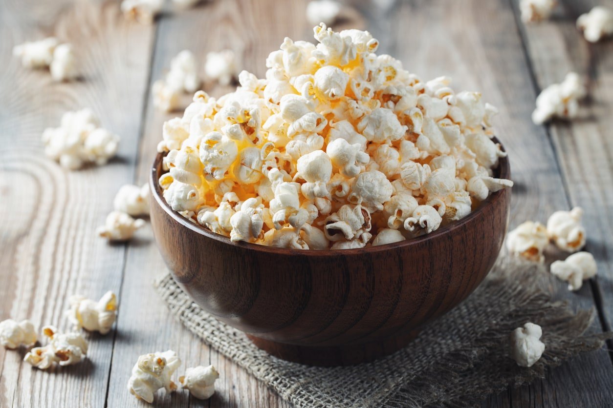A wooden bowl of salted popcorn at the old wooden table.