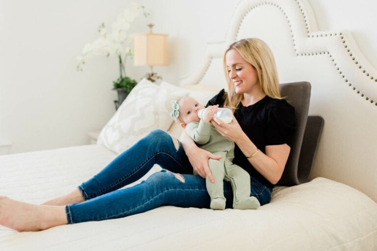 Woman sitting on the bed feeding her baby a bottle using the Ready Rocker.