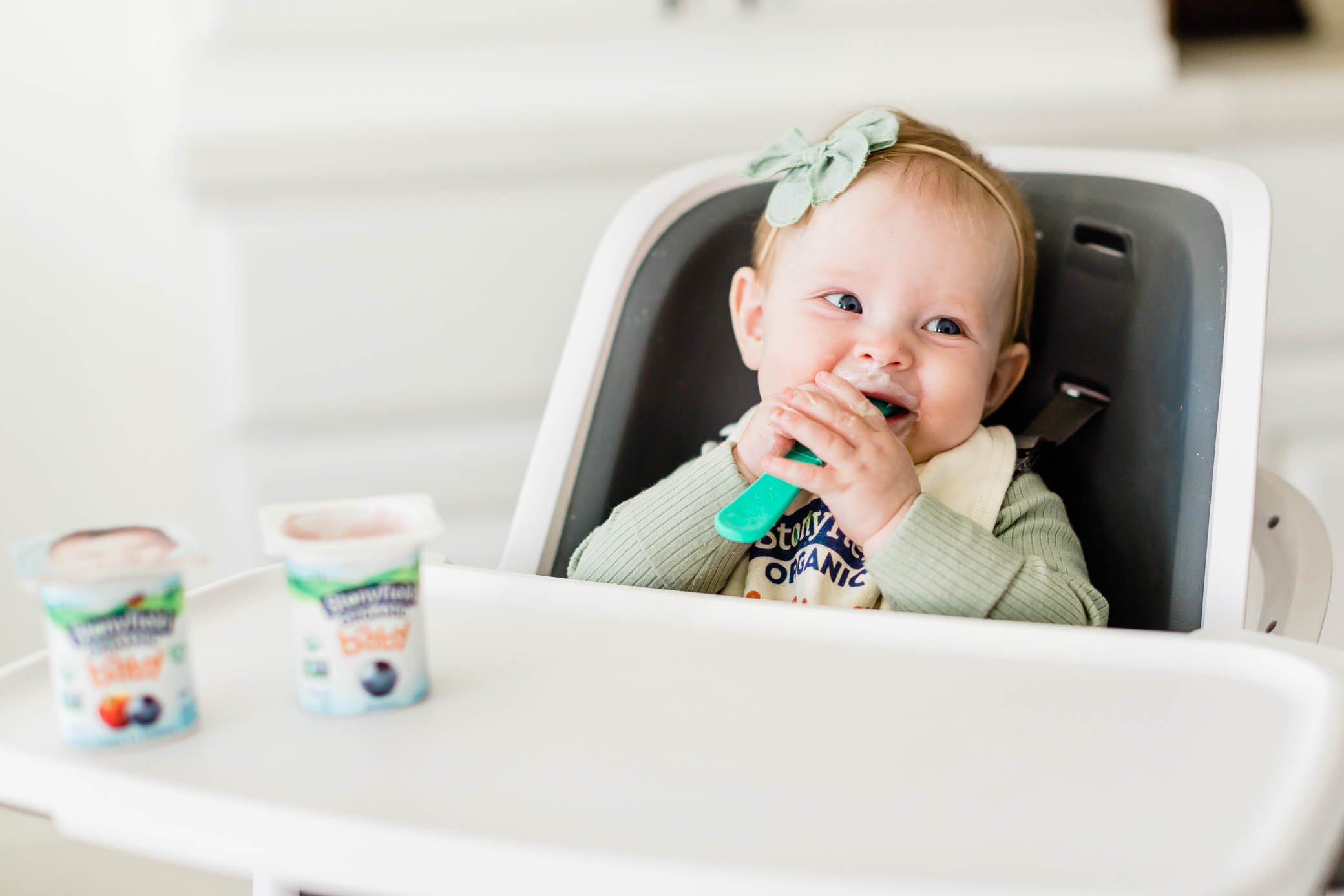 Baby girl sitting in her highchair eating Stonyfield Yobaby yogurt.
