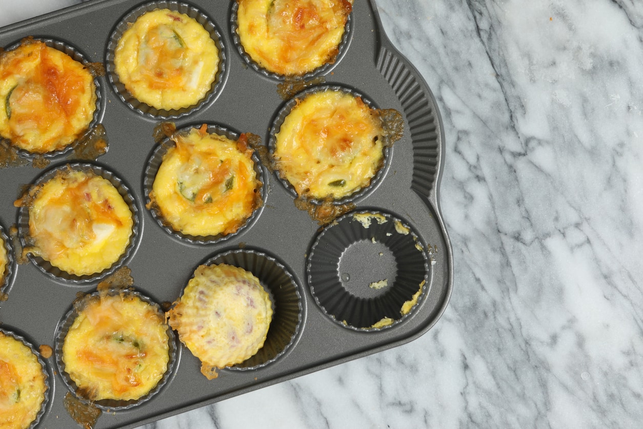 An overhead close up horizontal photograph of a baking pan with freshly made egg bites, it appears the chef has already sampled one of them.