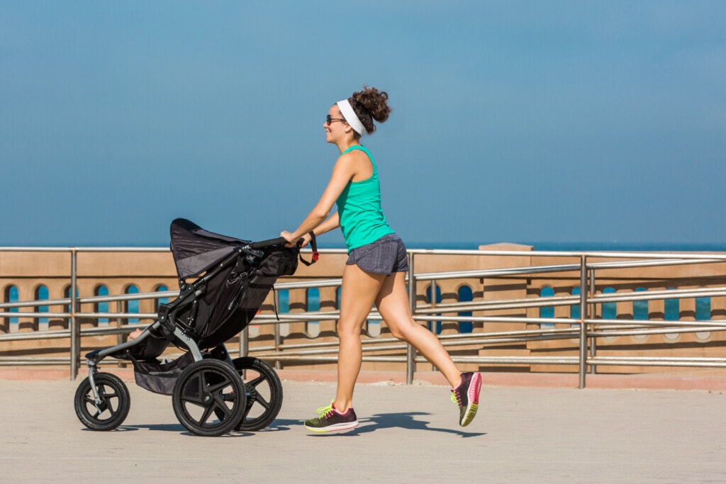 Fit mother jogging on a boardwalk with baby stroller.