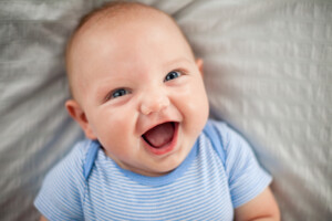 Color photo of a laughing baby boy lying on his back on a textured blanket.