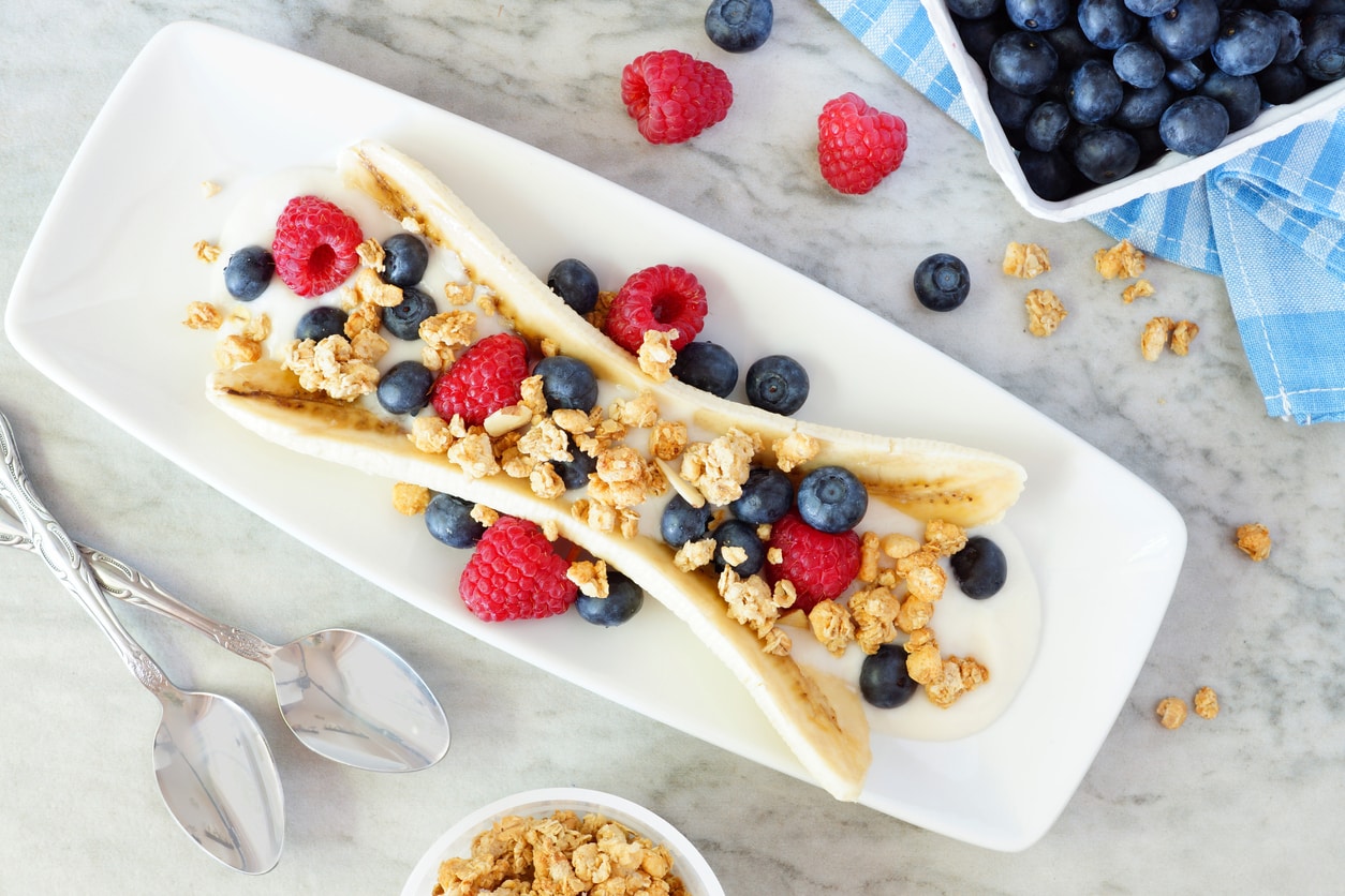 Healthy banana split with yogurt, fresh berries and granola, overhead scene on marble