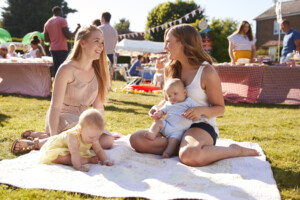Two Mothers With Babies On Rug At Summer Garden Fete