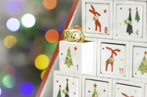 Close-up of the first compartment of a wooden advent calendar showing a bear's head candy. Background with defocused light on Christmas tree.