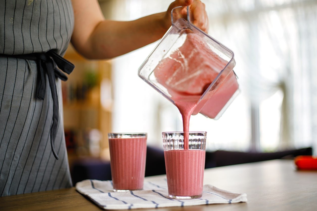 Young woman pouring Strawberry smoothie from blender