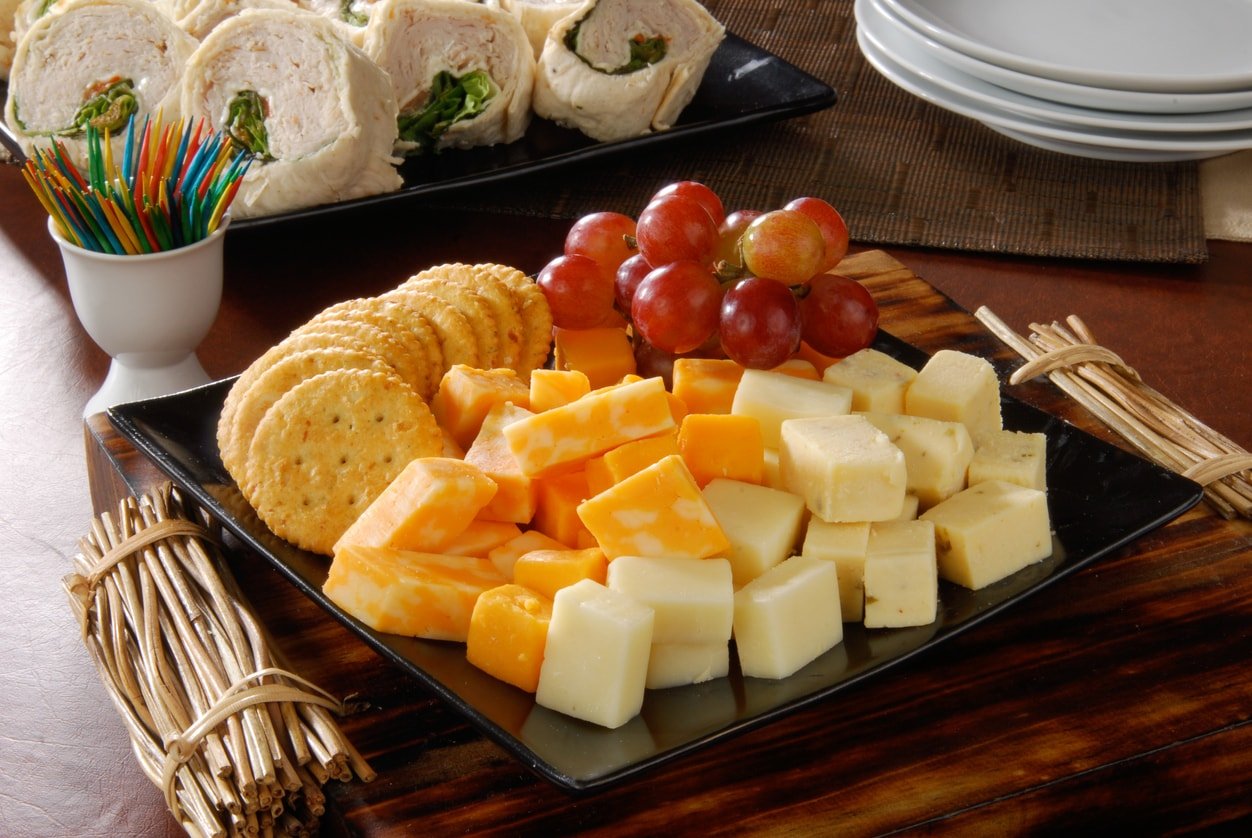A party tray of cheese and crackers and turkey wraps in the background