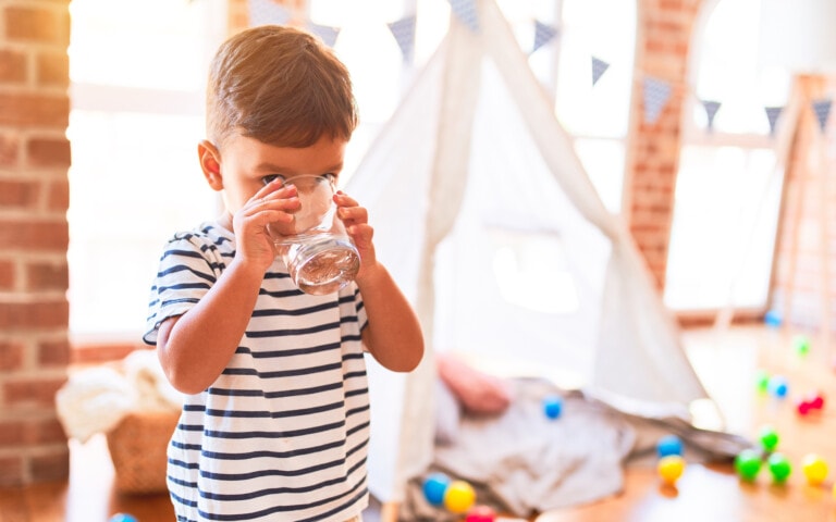 Sweet toddler boy drinking glass of water at kindergarten