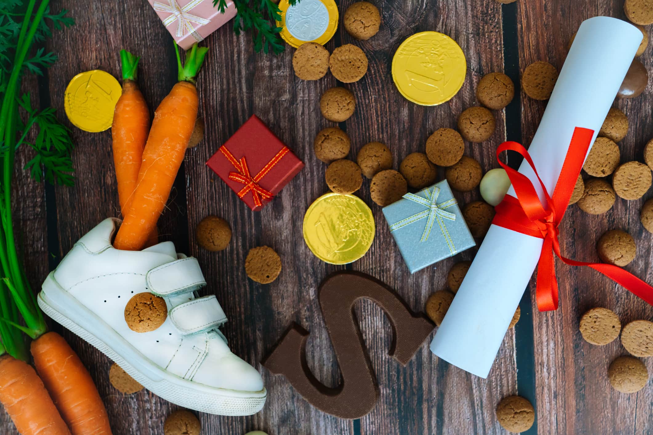 Dutch holiday Sinterklaas background with children shoe, carrots for Santa's horse, gifts, traditional sweets pepernoten and chocolate letter. Flat lay with copy space.