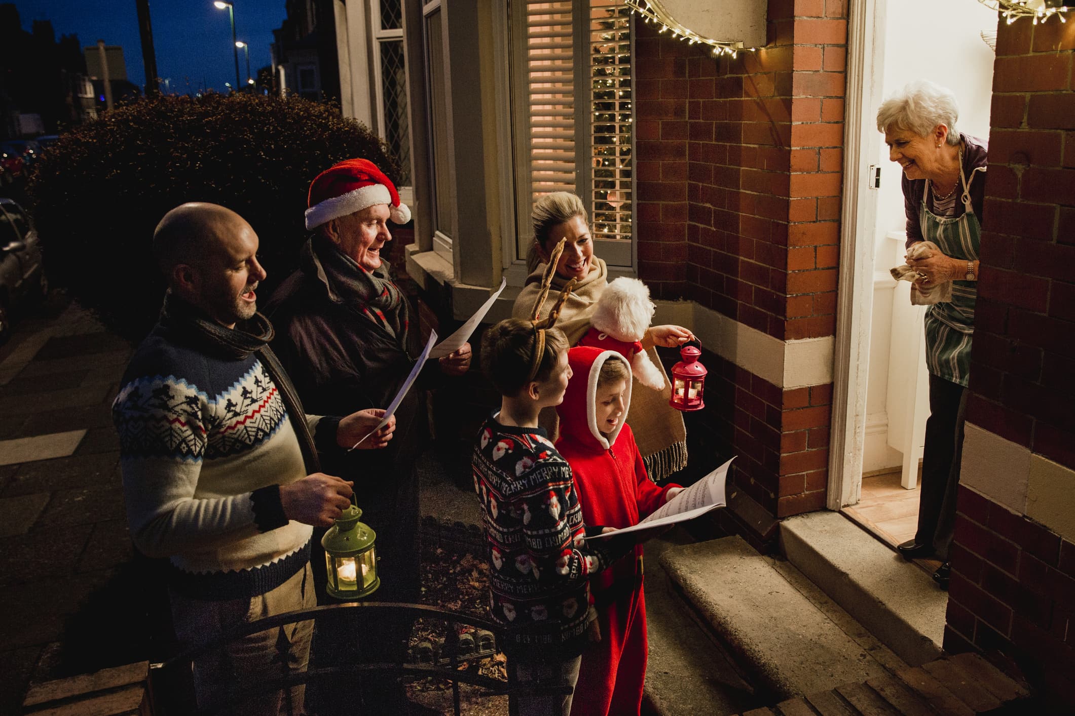 Three generation family are doing door-to-door carol singing. There is a senior woman at the door, appreciating their singing.