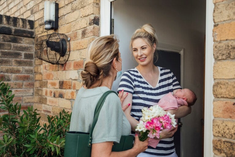 A shot of a grandmother wearing a protective face mask visiting her daughter and granddaughter with a special gift of flowers, they are greeting at the front door.