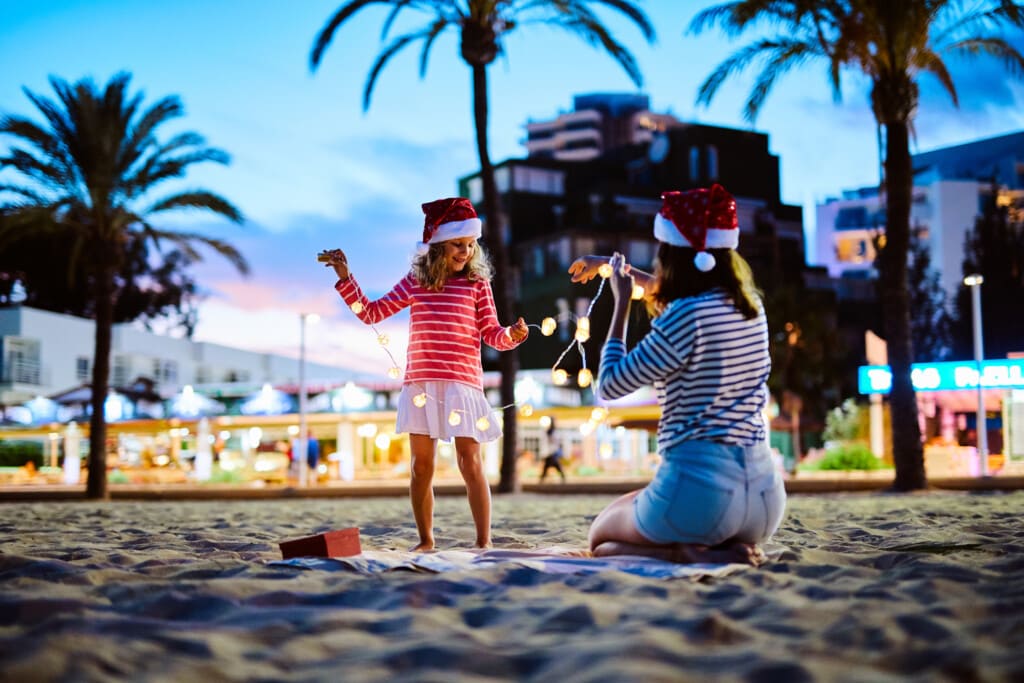 Mother and daughter wearing santa hats playing with christmas lights on the beach