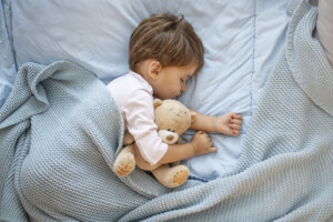 Boy sleeping on bed with teddy bear.