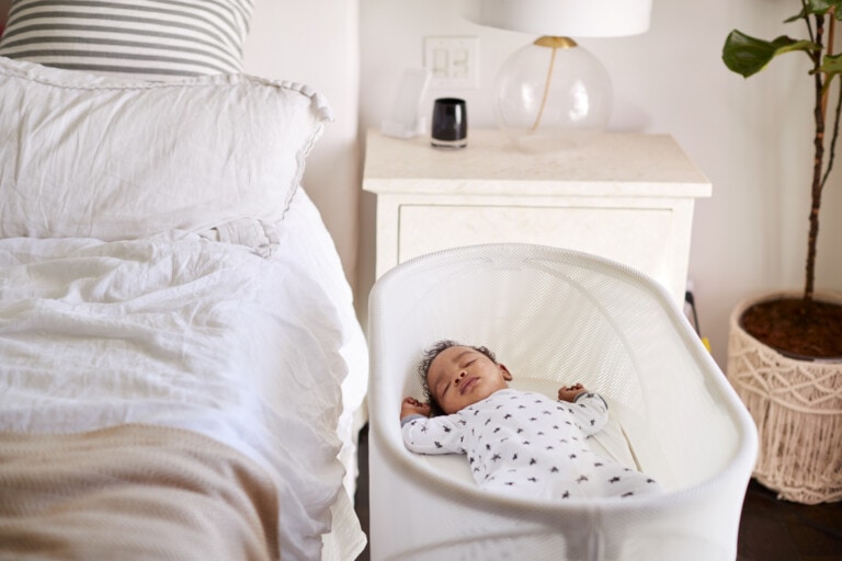 Three month old baby asleep in his cot beside the bed in his mother's bedroom