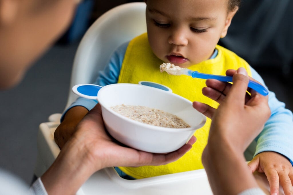african american mother feeding little son porridge or rice cereal at home