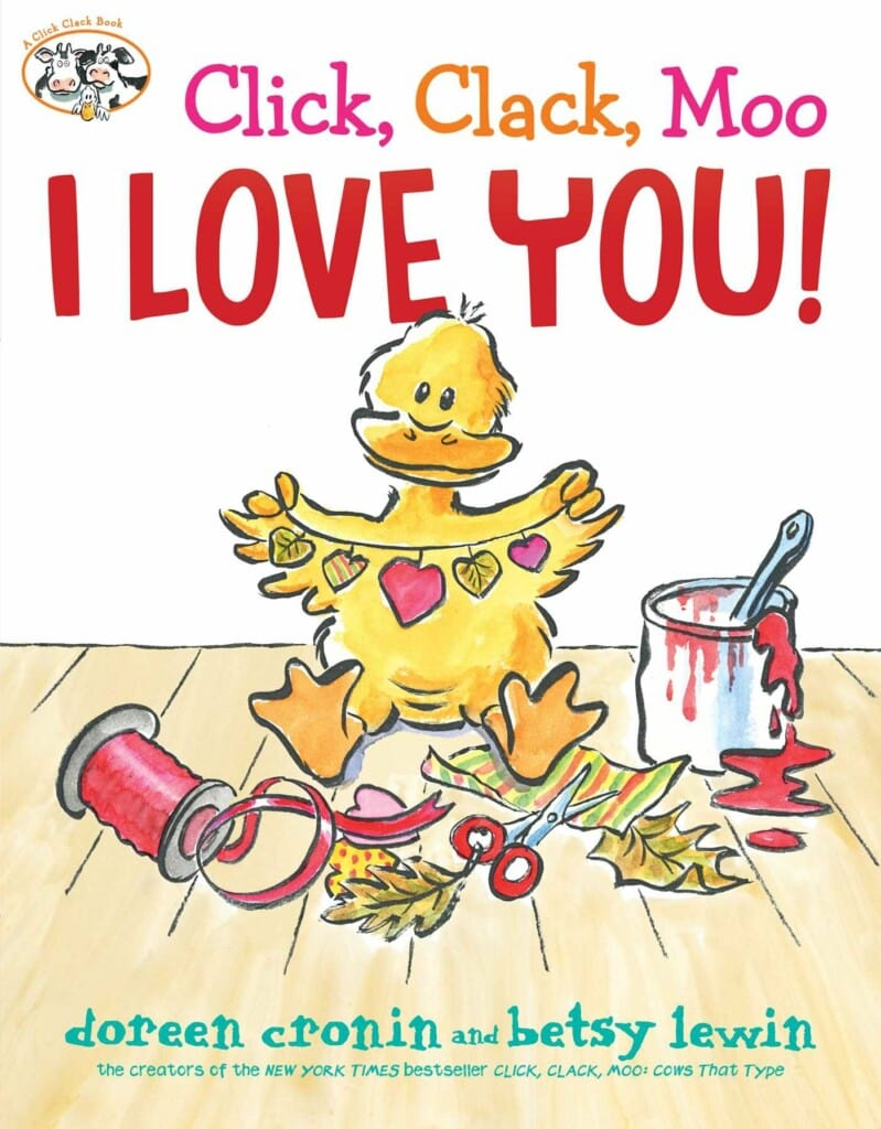 A duck holding up a heart garland sitting on the floor next to art supplies 